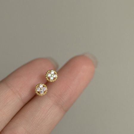 Gold version of the four-leaf clover stud earrings held between fingers to show scale.