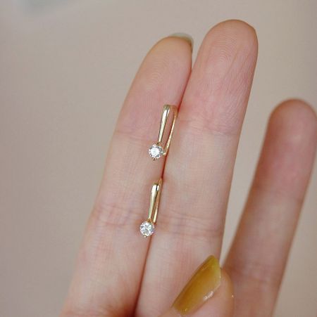 Detailed shot of the gold threader earrings held to display the zircon stones.