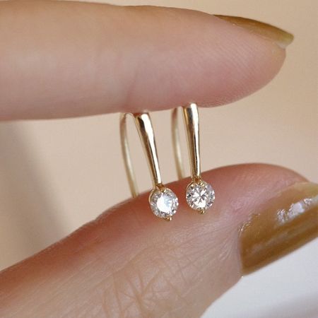 A hand holding a pair of 14K gold plated sterling silver hook earrings with crystal details.