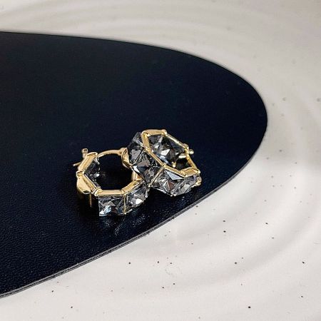 A pair of gold earrings with clear gemstones displayed on a white surface.