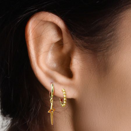 Close-up of a gold bead hoop earring worn on an ear, styled with another charm earring.