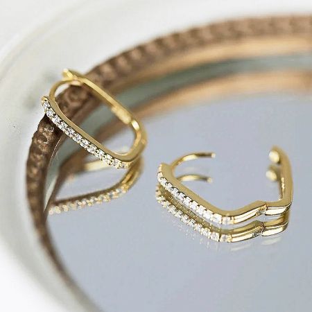A pair of gold rectangle huggie earrings with brilliant diamond accents on a white background.