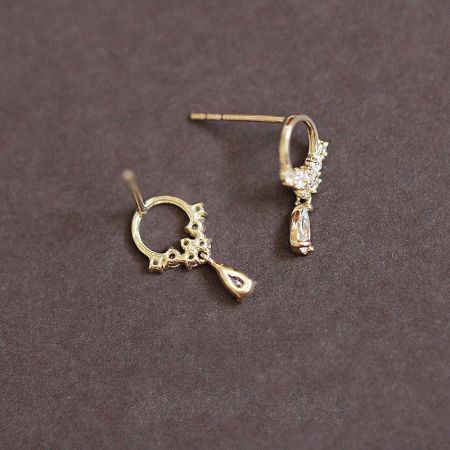 A pair of gold-plated teardrop earrings with white zircon gemstones, highlighting the intricate charm design.