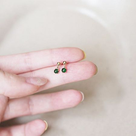 A hand holding a pair of minimalist sterling silver jade earrings to display their size and delicate design.