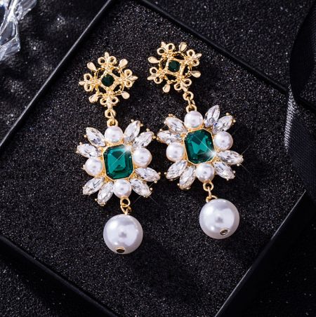 Close-up of the gold-plated dangle earrings, highlighting the vibrant emerald glass and lustrous faux pearls.