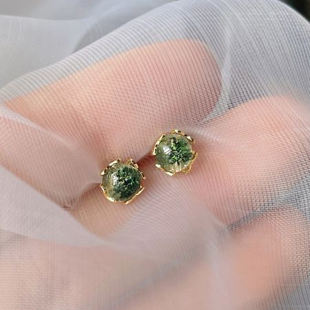 Detailed view of a pair of gold stud earrings with vibrant green stones.