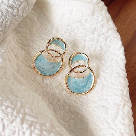 The gold and blue enamel earrings displayed on a textured white fabric.