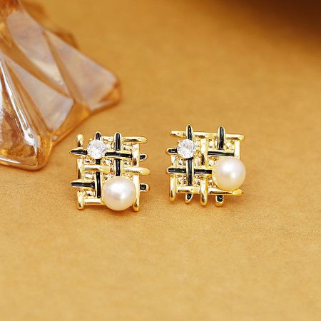 Close-up of the crisscross pattern on the gold stud earrings with pearl and gemstone.
