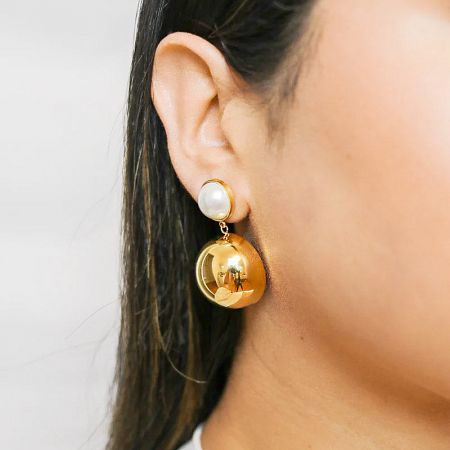 Studio shot of the pair of gold earrings, showing the pearl stud and dangling dome.