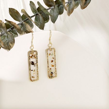 Detailed close-up view of the gold earrings, highlighting the transparent resin and embedded natural shell fragments.