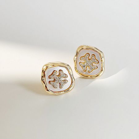A pair of gold stud earrings featuring a white mother-of-pearl design with clear stone accents.