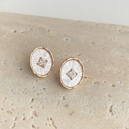 Close-up view of the gold stud earrings highlighting the white inlay and central clear gemstone.