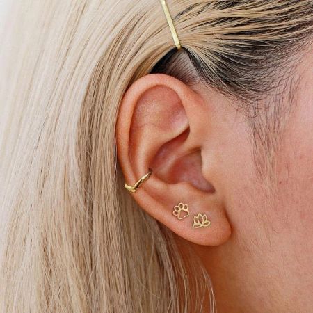 A gold version of the paw print stud earring shown on an ear with other jewelry.
