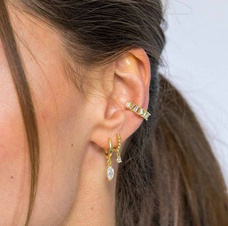 Close-up view of the three gold huggie hoop earrings on a woman's ear.