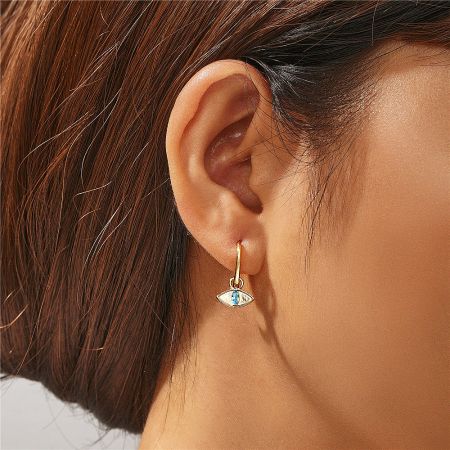 Close-up view of the gold evil eye huggie earring worn on an ear.