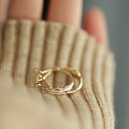 Product shot of the gold feather hoop earrings with cubic zirconia accents.