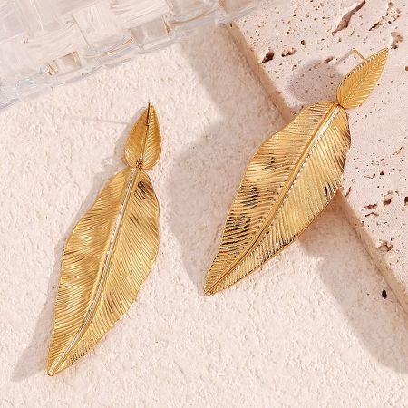 The gold feather earrings showcased on a textured pink stone.