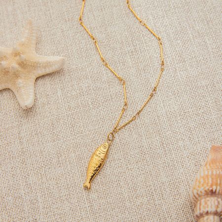The gold fish pendant necklace shown up close, emphasizing its beach-themed aesthetic.