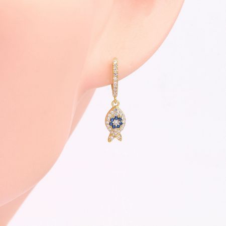 Detailed view of a gold fish-shaped earring pendant featuring white and blue stones on a delicate hook.