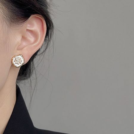 Close-up of a woman wearing a gold and white floral stud earring.