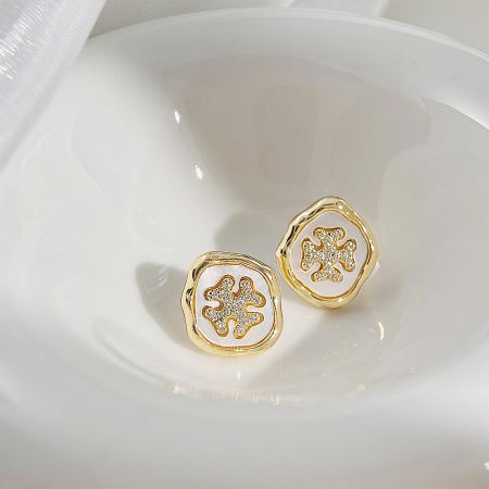 A pair of gold earrings with an intricate floral design and a central clear stone.