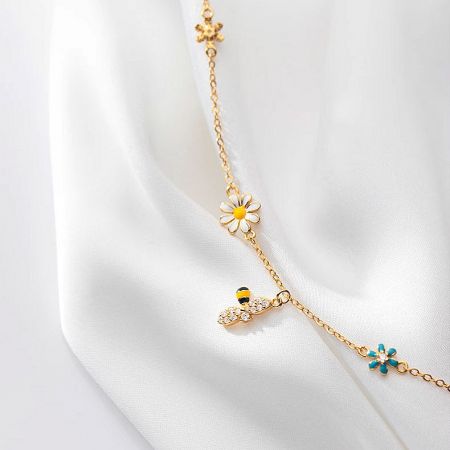 The gold-plated charm bracelet with daisy and bee charms laid out to display its full design.