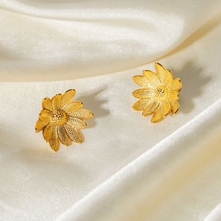 A pair of gold sunflower earrings elegantly displayed on a soft, satin background.