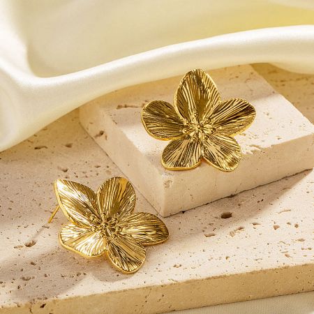 Product shot of the gold plated flower earrings resting on a textured stone surface.