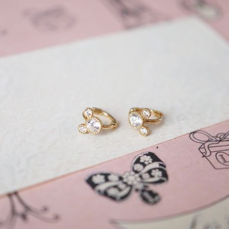 Product shot of the sterling silver huggie earrings with flower-like CZ stone arrangement on a pink butterfly-themed background.