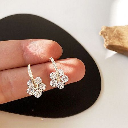 Hand holding a pair of gold flower earrings with sparkling crystals.