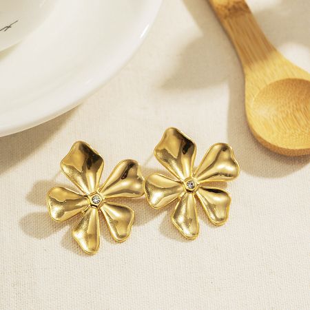 A pair of gold flora flower stud earrings with sparkling diamond-like centers on a white background.