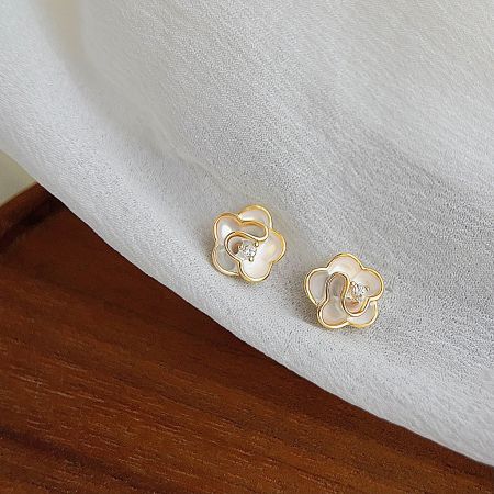 Product shot of the gold flower earrings with sparkling zircon accents on a textured background.