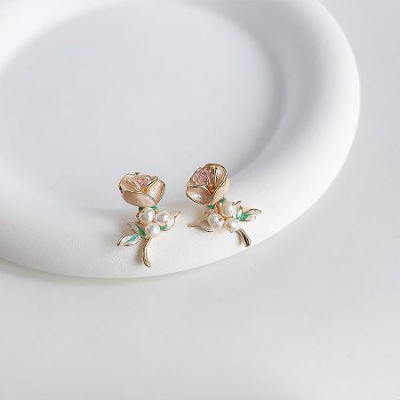 The enamel rose flower earrings displayed on a white platform, highlighting the pink and gold colors.