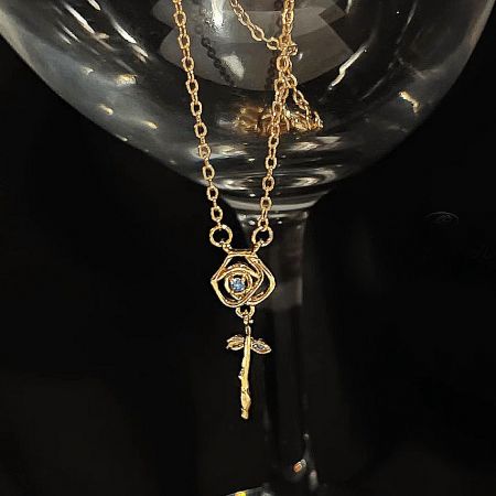 Artistic shot of the gold flower necklace with a blue gemstone, displayed on a glass goblet.