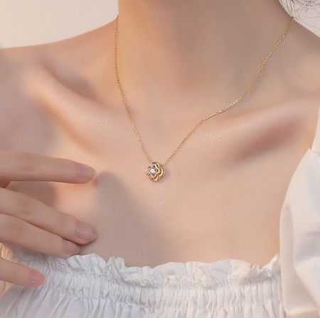 Detailed view of the gold clover leaf pendant necklace on a neutral background.