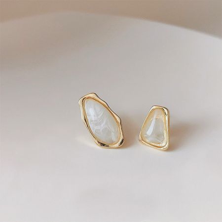 Product shot of a pair of gold-framed earrings with irregular white stones.