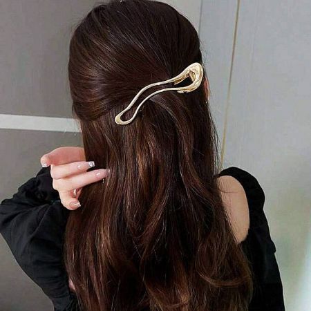 A stylish gold metal hair clip securing a half-up hairstyle on dark brown hair.