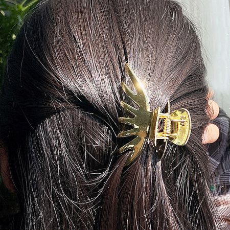 A woman with dark brown hair using the gold pumpkin-shaped hair clip to style a ponytail.