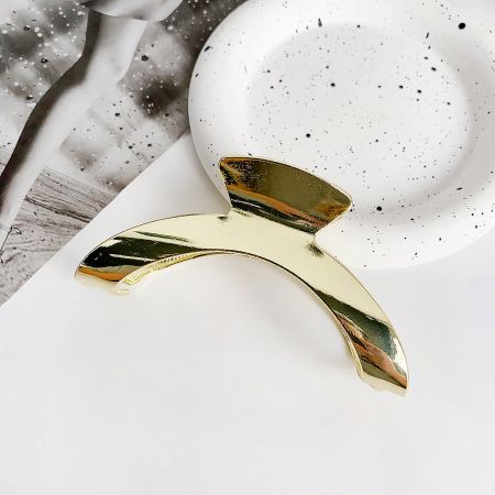 Detailed product shot of a gold metal curve-shaped shark claw hair clip.