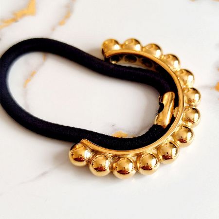 Close-up view of the gold hair tie, highlighting its smooth finish and black velvet strap.