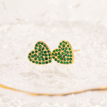 A close-up view of the gold pave green zircon heart stud earrings resting on a white crystal surface.