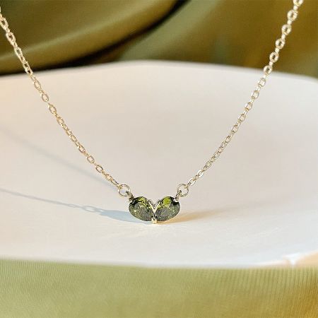 Gold Plated Green Emerald Heart Choker Necklaces (Set of 5) - Close-up of a gold-plated choker necklace with a delicate heart-shaped pendant holding two vibrant green emerald gemstones.