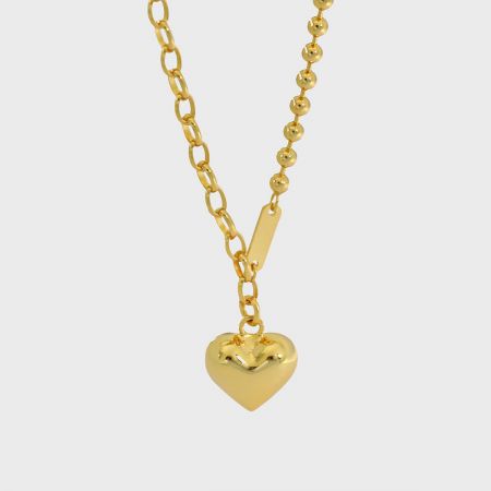 Detailed close-up of the gold-tone puffed heart pendant on a mixed beaded and link chain.