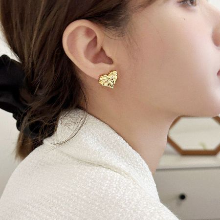 A close-up view of a woman wearing a gold irregular heart-shaped stud earring.