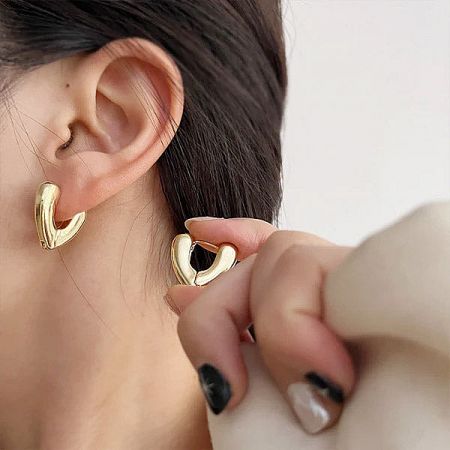 Woman elegantly putting on the gold V-shape sterling silver hoop earring.
