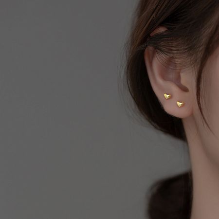 Close-up of a woman wearing a tiny gold heart stud earring.