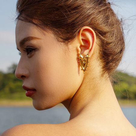 A model showcasing the stylish 18k gold-plated heart and sphere stud earrings.