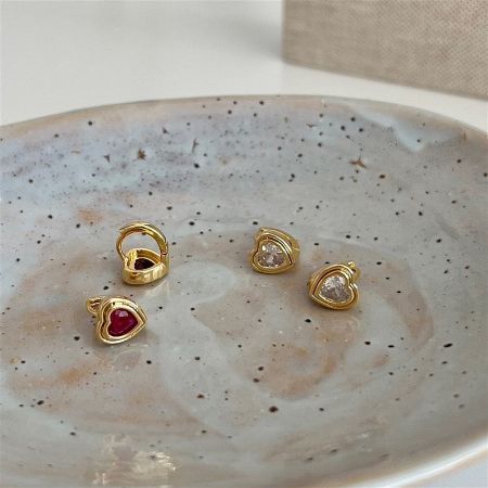 Four pairs of gold heart-shaped huggie earrings displayed on a decorative speckled plate.