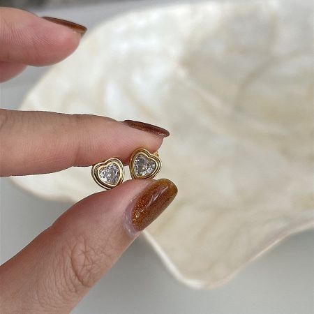 A close-up of a hand holding the gold heart-shaped earrings with clear cubic zirconia.