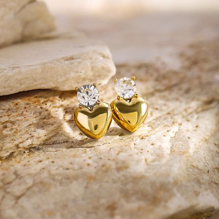 Close-up view of the pair of gold heart-shaped earrings with clear gemstones.